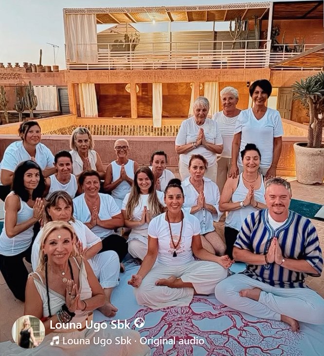 Groupe de participants à la retraite yoga sur le rooftop du Riad Vendôme Marrakech, en posture de namaste au coucher du soleil